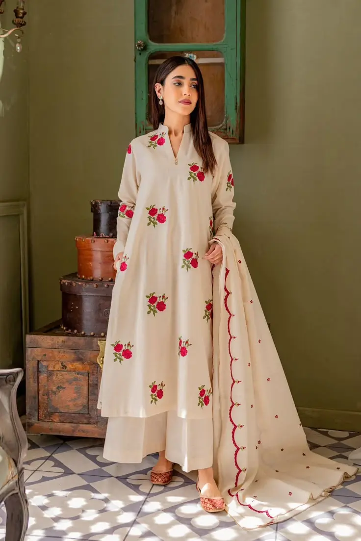 A woman in a cream embroidered suit adorned with red roses, showcasing elegant floral details party wear dresses for women in kerala