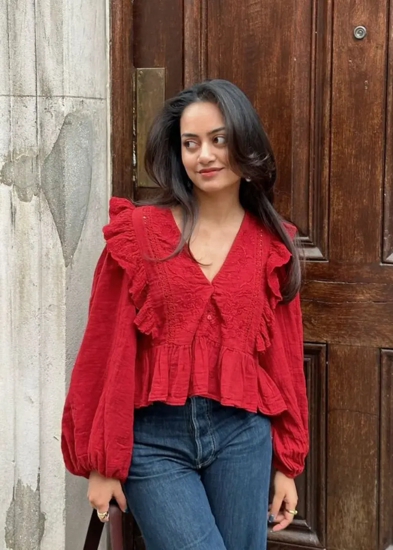  A woman wearing jeans and a red blouse stands confidently, showcasing a casual yet stylish outfit women's shirts in kerala